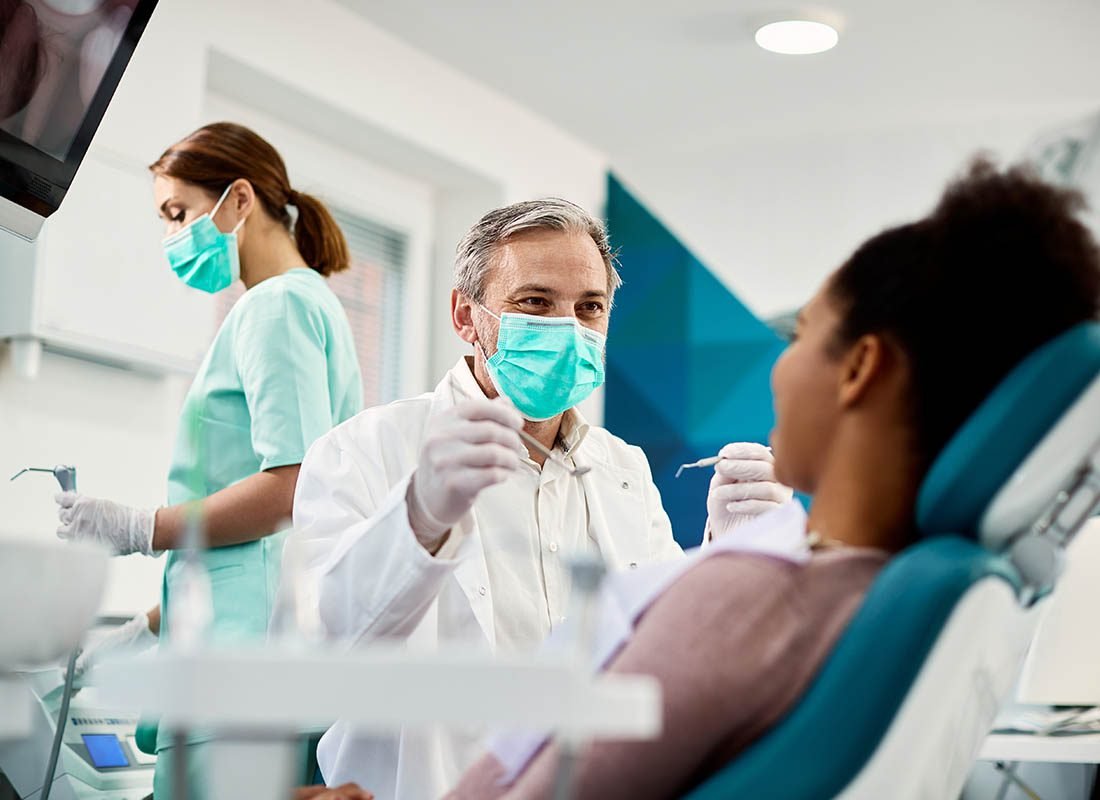 Group-Dental-Insurance-Woman-Getting-Her-Teeth-Cleaned-by-a-Dentist-and-an-Assistant